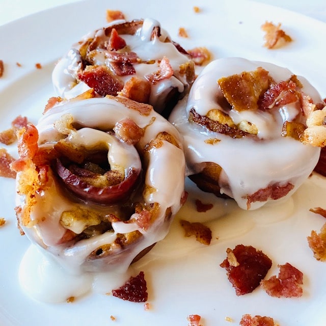 Cinnamon rolls with crumbles of bacon on white plate.