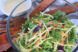 Kale Salad in glass bowl with wooden serving utensils