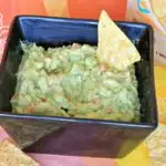 Black square bowl full of fresh guacamole with tortilla corn chip