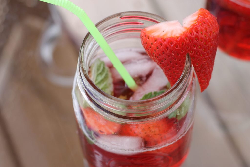 Mason jar glass with strawberry cocktail, green straw and fresh strawberry on the rim. 