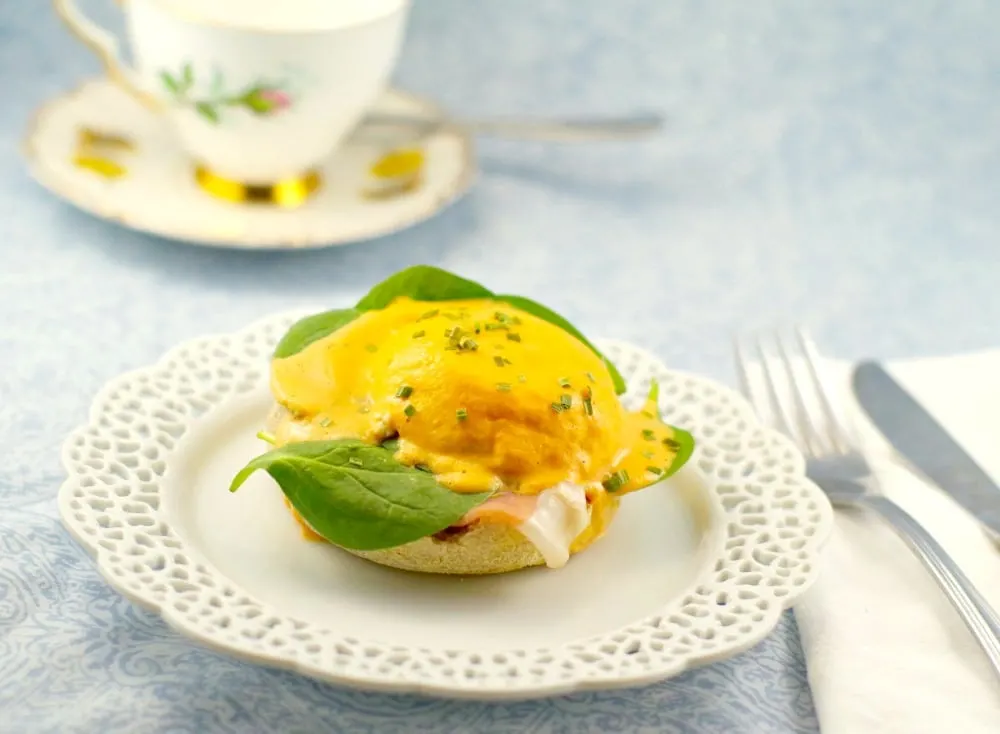 Eggs benedict on white plate with tea cup behind