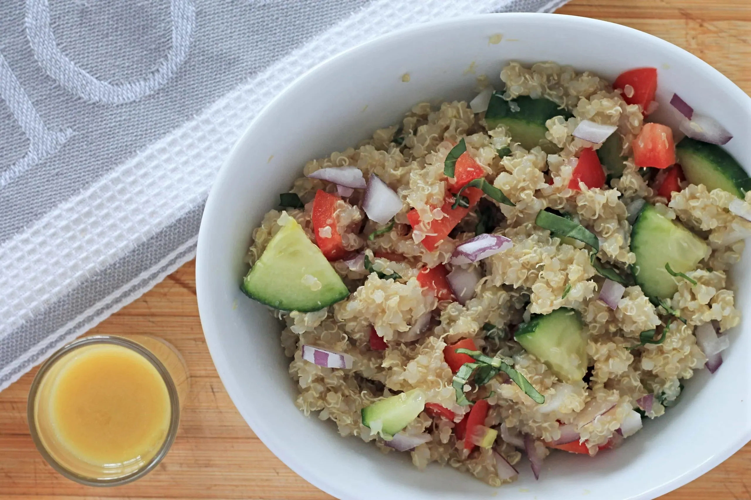 Quinoa salad in white bowl on wooden cutting board with small dish of lemon dressing