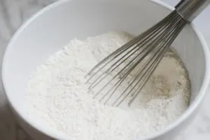 White ceramic bowl with dry ingredients and whisk