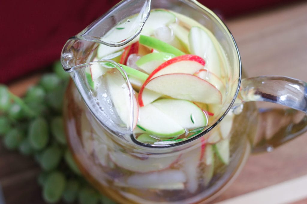 White sangria in clear glass pitcher with fresh cut apples and grapes