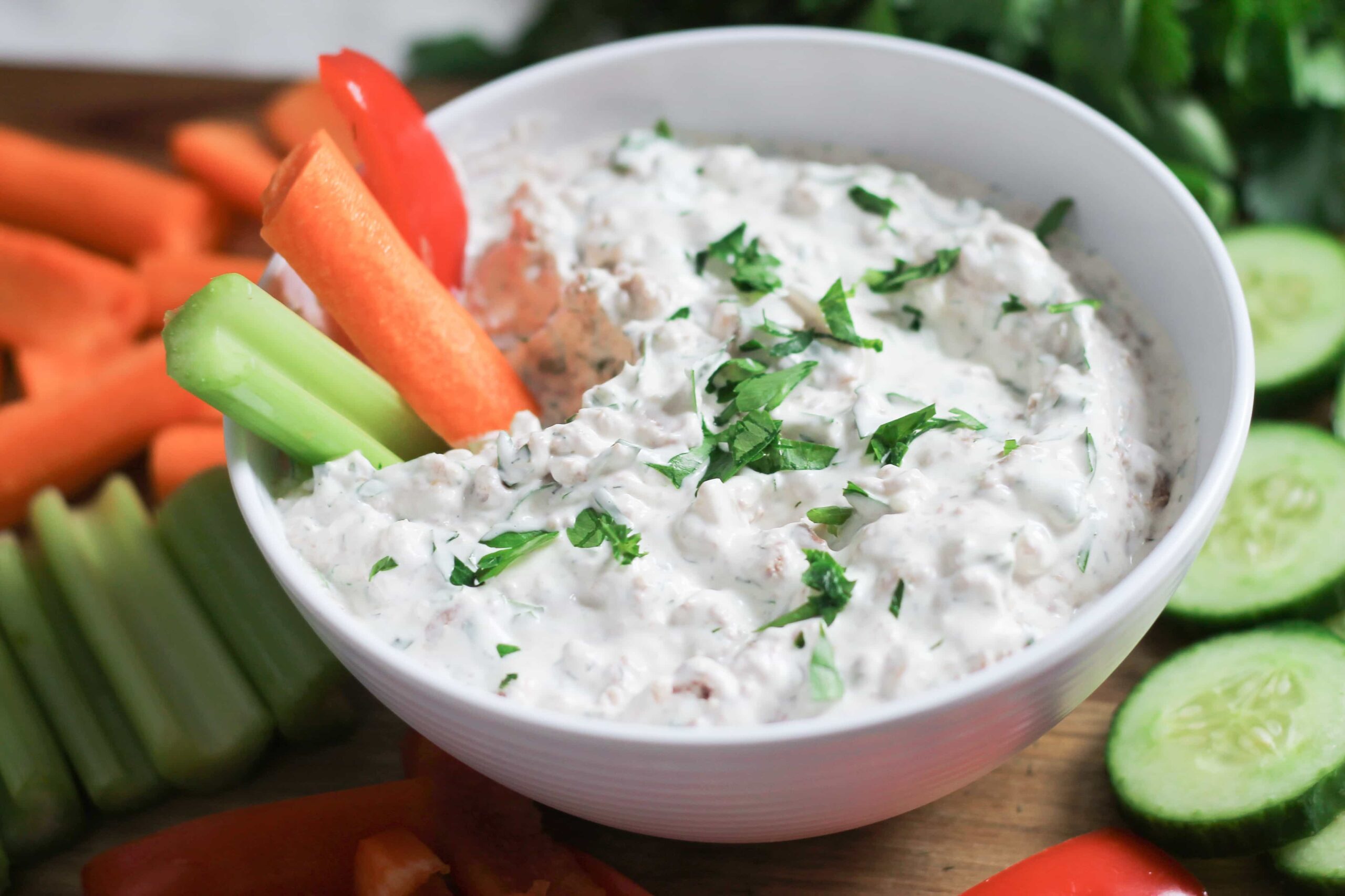 White bowl full of corned beef veggie dip on cutting board with fresh cut carrots, celery and cucumber