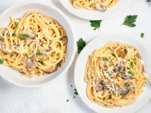 Plates of mushroom pasta on white table