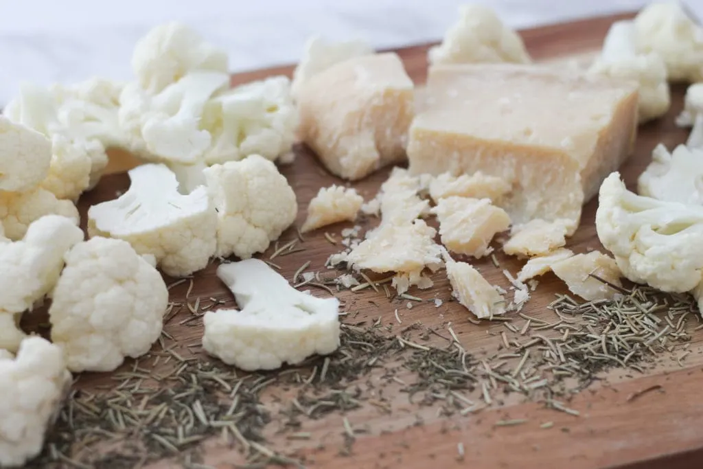 sliced cauliflower florets on cutting board with herbs and Parmesan 