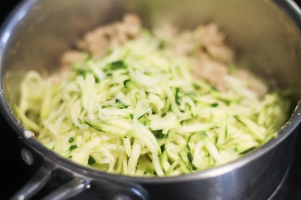 Pot on stove with grated zucchini and italian sausage 