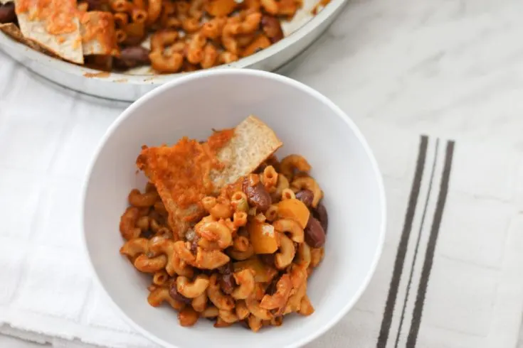 White bowl with Chili Mac on top of tea towel with a stainless steel skillet in the background