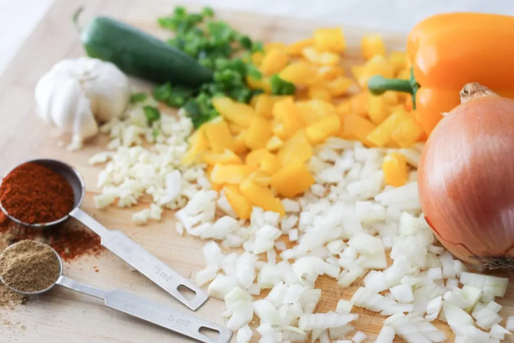 Chopped onions and Bell Peppers on cutting board with garlic, jalapeno and spices