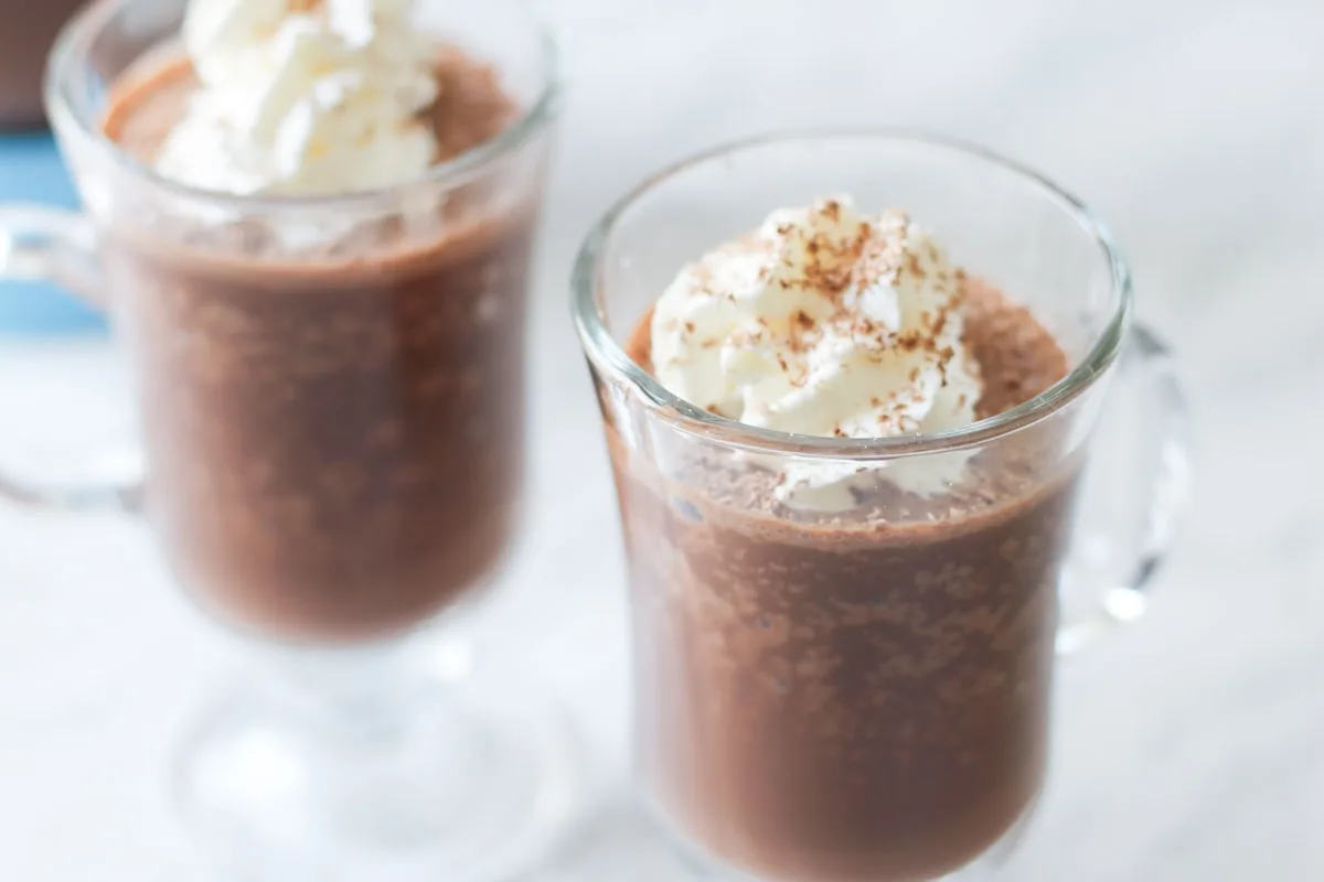 Two clear mugs filled with frozen hot cocoa and topped with whipped cream