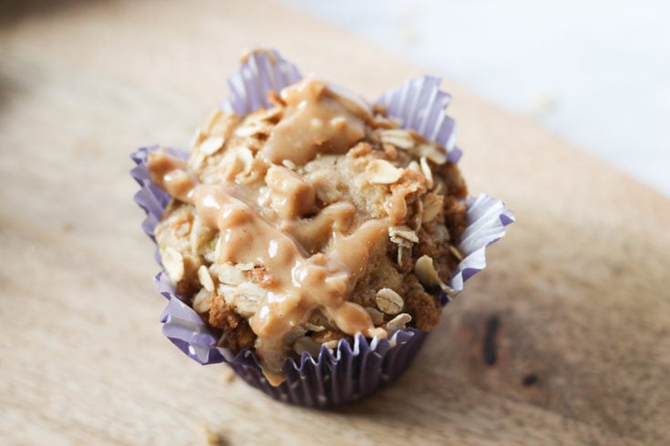 Freshly baked apple muffin in purple muffin liner on wooden cutting board