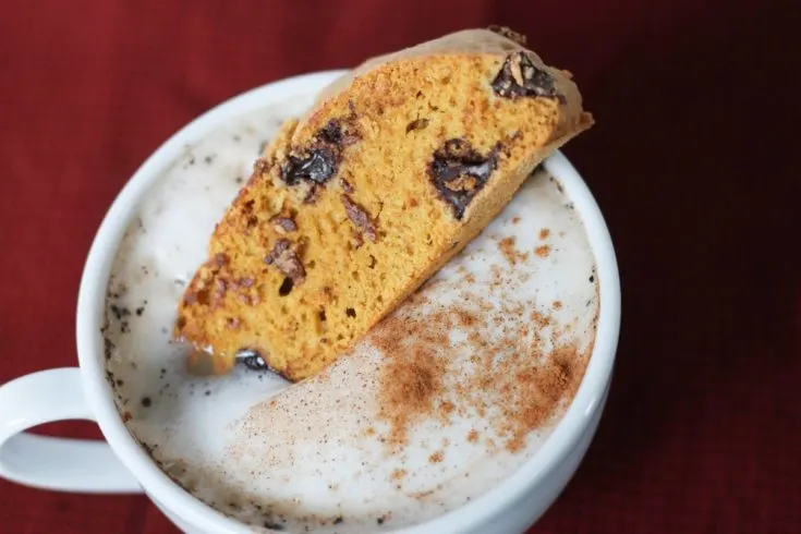 Pumpkin Biscotti dunked in frothy cappuccino on red tablecloth