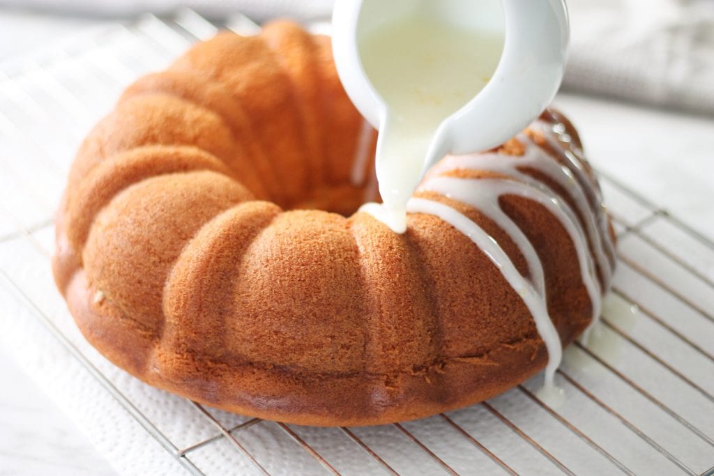 Lemon bundt cake being drizzled with fresh lemon glaze over a metal cooling rack.