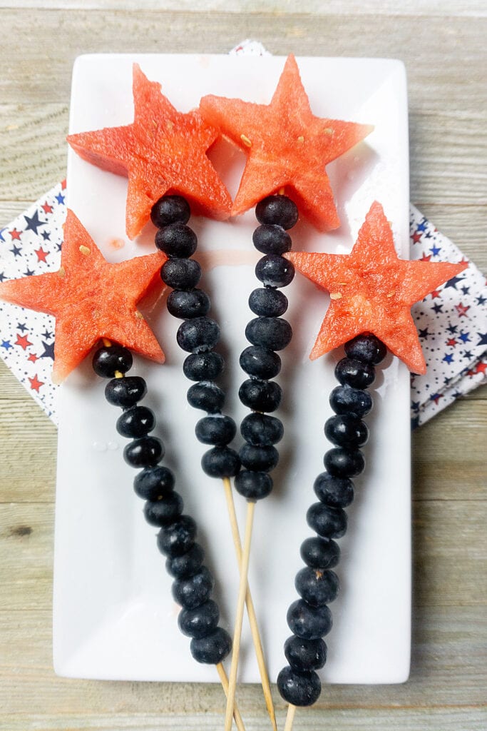 White plate with 4 fruit skewers on top of napkin.