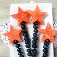 4 watermelon and blueberry fruit skewers on white rectangular tray with napkins underneath.