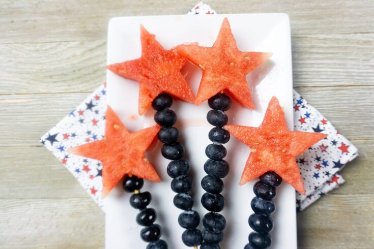 4 watermelon and blueberry fruit skewers on white rectangular tray with napkins underneath.