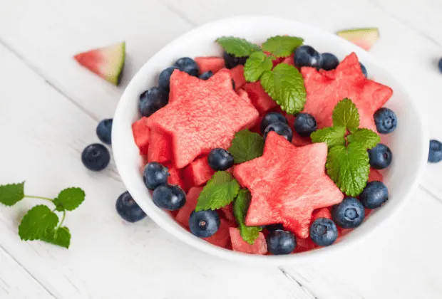 White bowl with star shaped watermelon slices and fresh blueberries on white countertop.