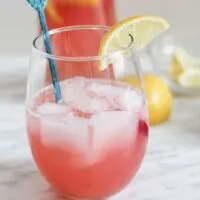 Glass of rhubarb lemonade with stir stick and lemon wedge on counter top.