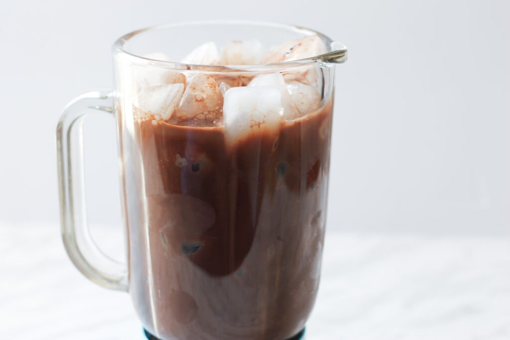 Blender on countertop with ice and chocolate syrup mixture