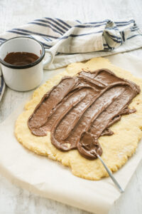 Rolled out dough on parchment with a spoon of Nutella spread in the center.