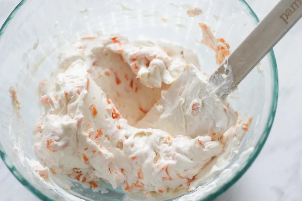 Glass bowl with mixture of cream cheese and cheddar cheese with white spatula. 