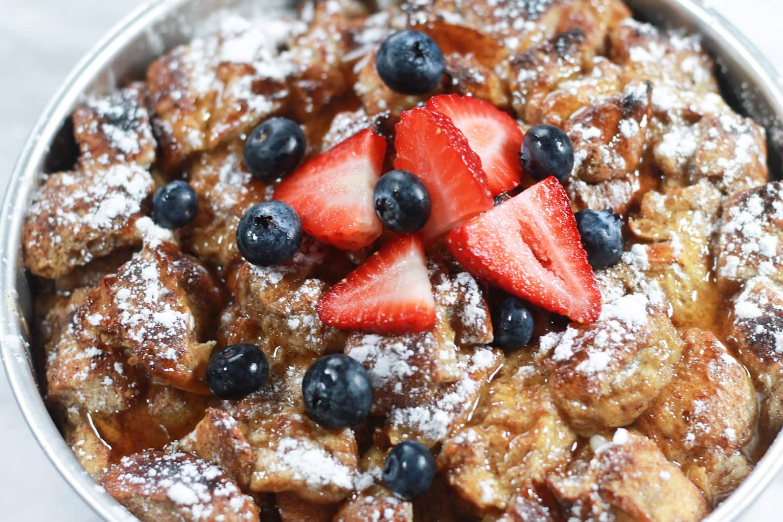 Baking pan with French toast casserole, topped with fresh berries and powdered sugar.