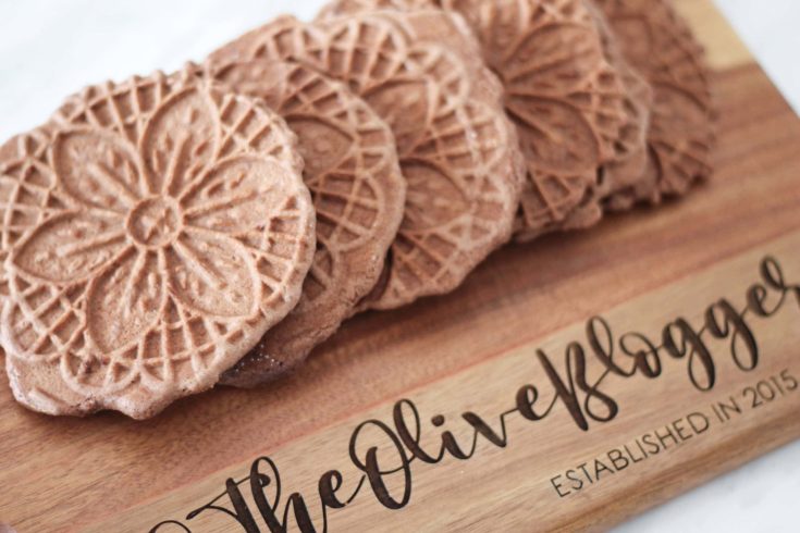 Wooden cutting board with chocolate pizzelle cookies laid across.